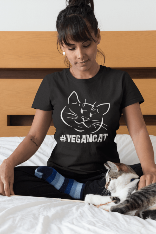 woman wearing a hashtag vegan cat t-shirt petting her cat on bed